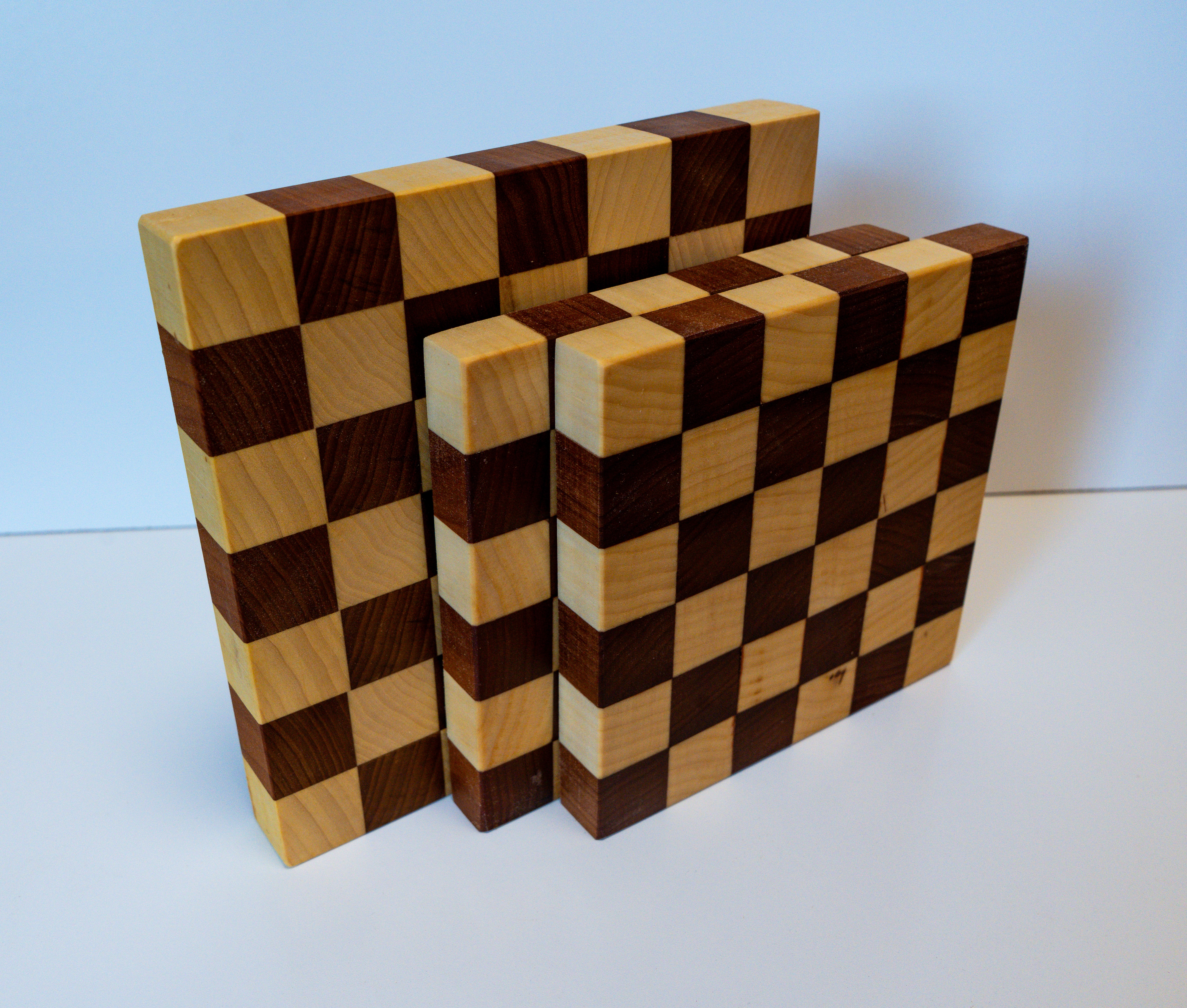 Three handcrafted wooden cutting boards arranged in a stack, featuring a checkerboard pattern of light and dark wood.